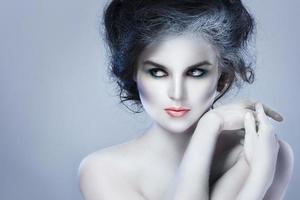 Woman in white body-art in creative image of winter, snow queen, or another sad or evil character photo