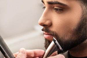 Hairdresser is shaving beard with a hair-clipper photo