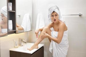 Woman is shaving her legs after shower photo