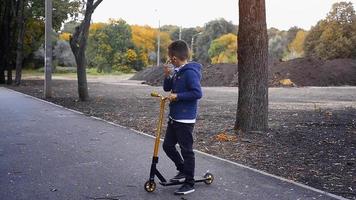 giovane ragazzo cavalcate su un' scooter a il autunno parco video