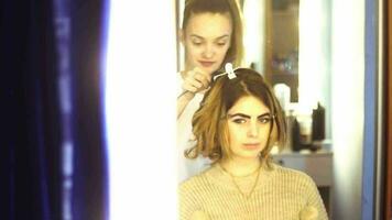 la estilista rubia hace el peinado a una mujer joven en el estudio del cabello video