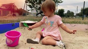 una niña bonita juega en un arenero con juguetes en horario de verano en 4k video