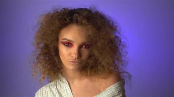 mooi jong meisje met pluizig gekruld haar- en kleurrijk bedenken in studio Aan Purper achtergrond in langzaam beweging video