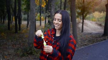 alegre mujer morena adulta soplar burbujas en el parque en el cálido día de otoño video