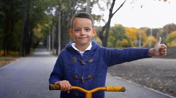 jeune garçon sur un scooter regardant la caméra et montrant les pouces vers le haut à la chaude journée d'automne