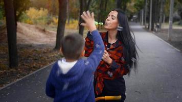 mãe morena adulta sopra uma bolha com seu filho no parque em um dia quente de outono video