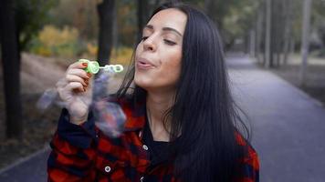 Fröhliche erwachsene brünette Frau bläst am warmen Herbsttag draußen im Park Blasen video