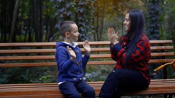 Mutter spielt mit ihrem kleinen Sohn auf einer Bank im Park an einem warmen Herbsttag. fröhliche Familienstunden. video