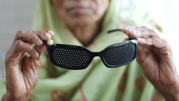 anciana sosteniendo gafas de sol médicas perforadas con agujeros para entrenar la visión