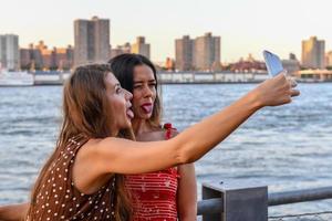 Two girls interacting with a mobile phone and taking silly selfie photos in New York City