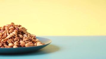 Processed peanuts on a plate on color background video