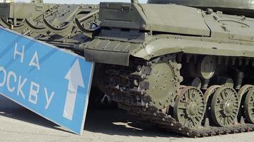 Blue road sign with white letters near the tank, on the territory of Ukraine. War of Russia against Ukraine. Transfer to Moscow.