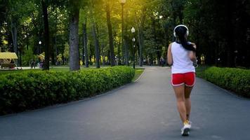 bella adulto giovane brunetta corridore donna praticante a il parco astuzia ascoltando musica a caldo estate sera video