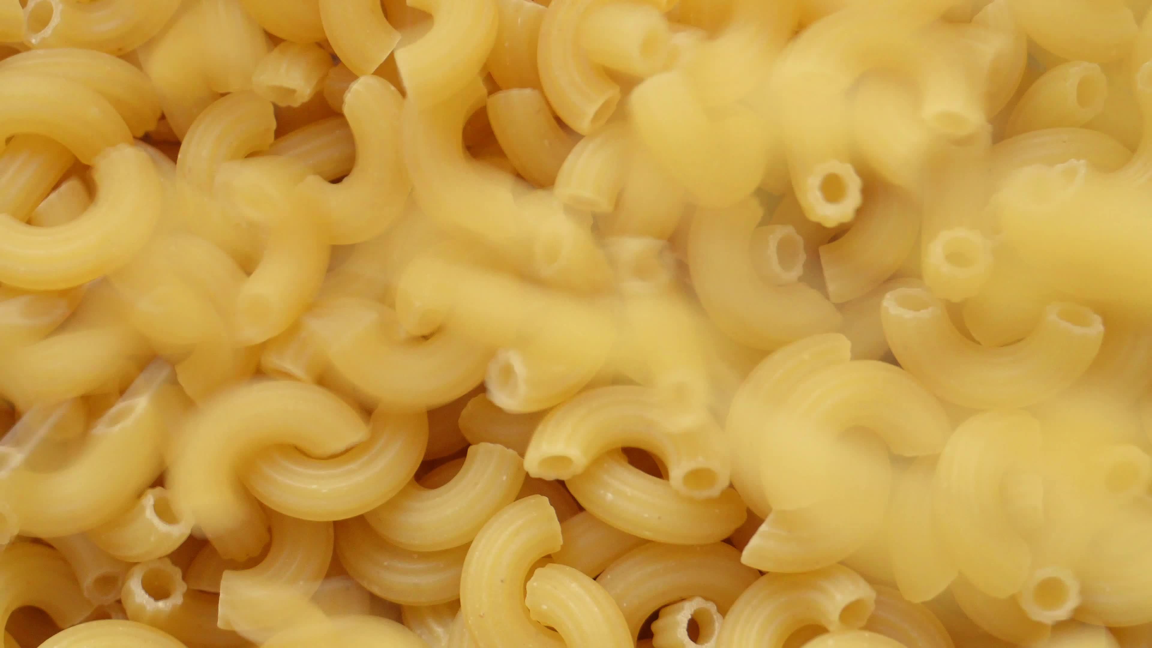 Uncooked elbow macaroni being poured into a heap of pasta full screen