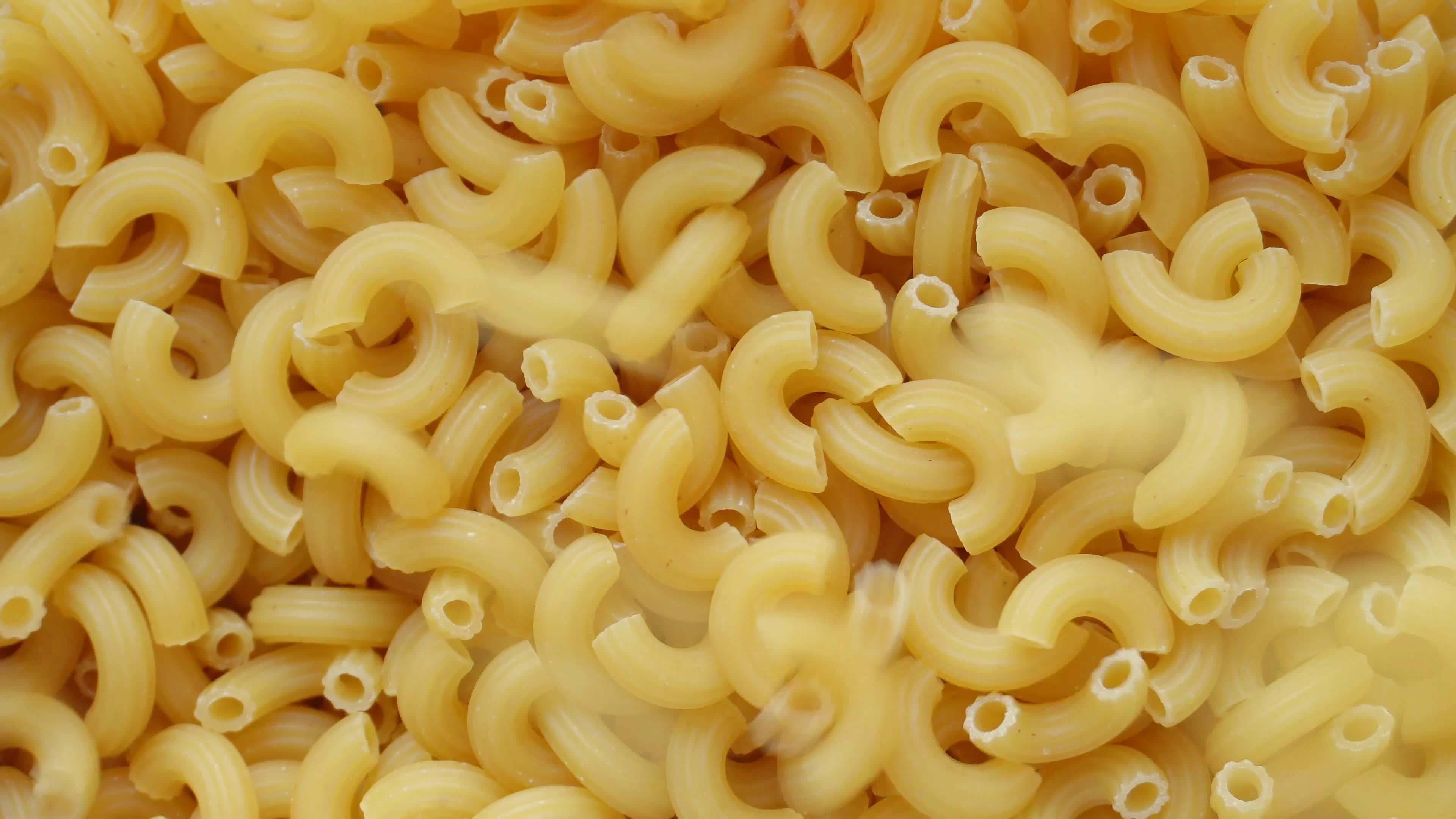 Uncooked elbow macaroni being poured into a heap of pasta full screen