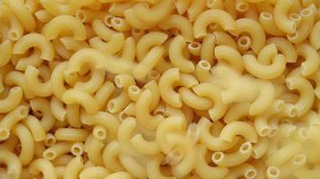 Uncooked elbow macaroni being poured into a heap of pasta full screen video