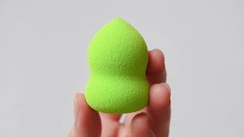 Hand holding a clean makeup sponge, plain white background. video