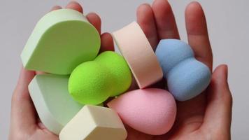 Female hands holding a lot of pastel makeup sponges of different colors and shapes on a plain white background. video