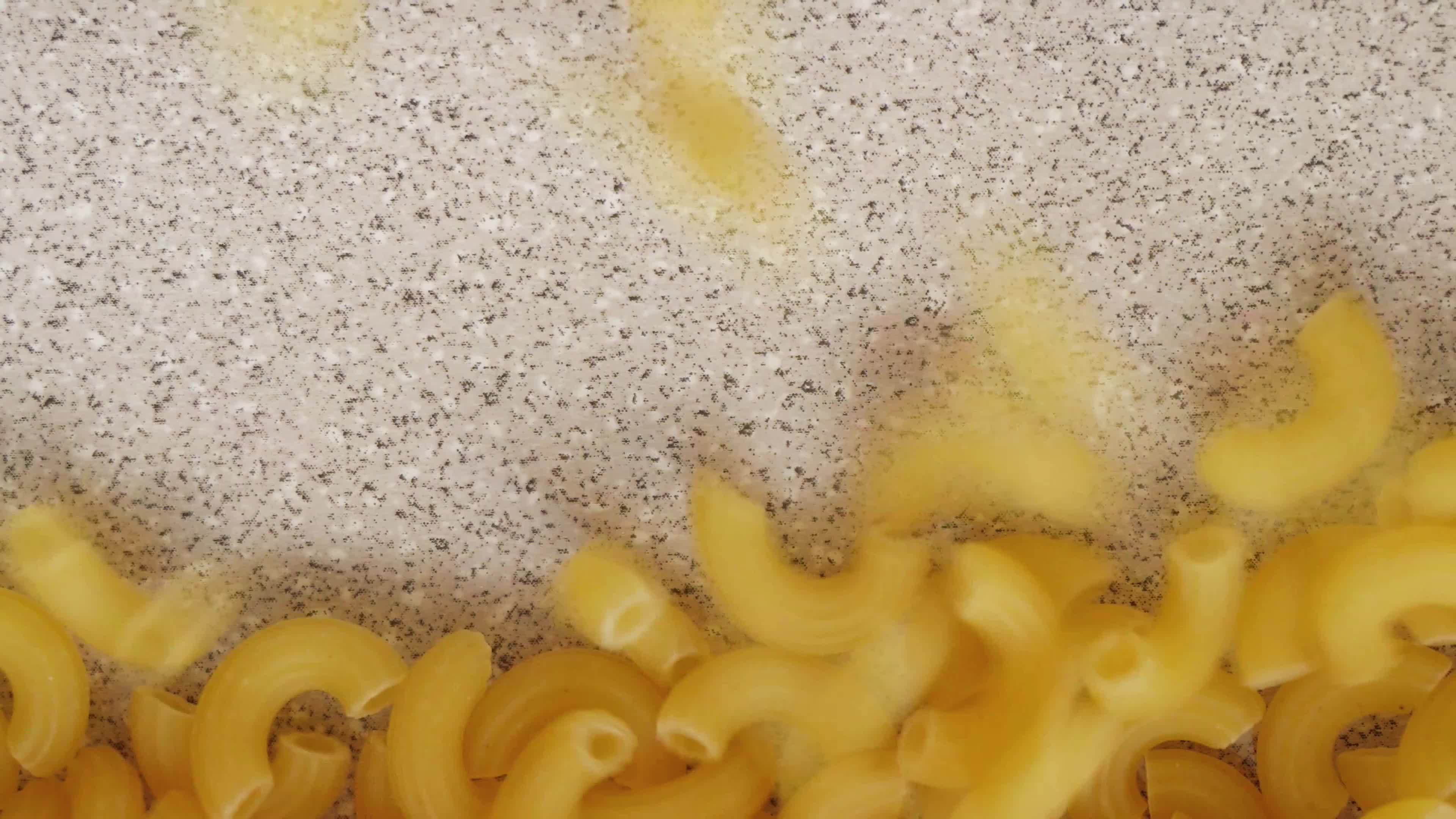 Uncooked elbow macaroni slowly being poured and filling up screen