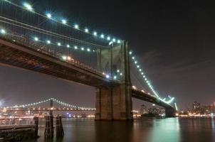 Brooklyn Bridge closeup over East River at night in New York City Manhattan with lights and reflections. photo