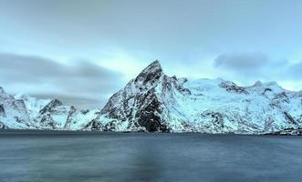 cabaña de pesca en el pico de la montaña hamnoy y lilandstinden en invierno en reine, islas lofoten, noruega. foto