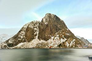 cabaña de pesca en el pico de la montaña hamnoy y lilandstinden en invierno en reine, islas lofoten, noruega. foto