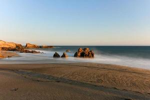 Impresionante vista de larga exposición de olas suaves que chocan contra formaciones rocosas al atardecer, punto sequit, playa estatal leo carrillo, malibu, california foto