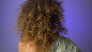 Beautiful young girl with fluffy curly hair and colourful makeup in studio on purple background in slow motion video