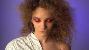 linda garota com cabelo cacheado fofo e maquiagem colorida em estúdio em fundo roxo em câmera lenta video