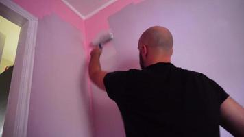 Mens verven de roze muren in de kamer naar magenta kleur met een verf rol video