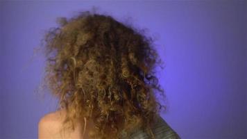 Beautiful young girl with fluffy curly hair and colourful makeup in studio on purple background in slow motion video