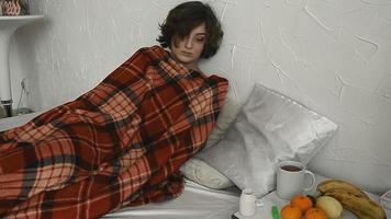 una mujer enferma yace debajo de una manta y mide la temperatura corporal en casa