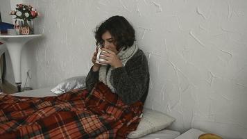 Sick woman lies in bed in a sweater with a hot drink at home video