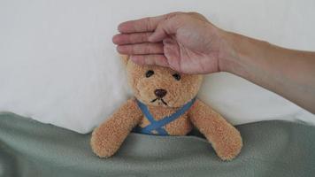 Concept of feeling sick and Fever. Using a bear as a child representation. Men measure head temperature with their hands and use a cooling gel to reduce fever. video