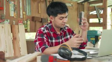 Asian man carpenter owns recheck wood and design. carpenter use mobile phone and discussing request from customer.Small business owner carpentry concept. video