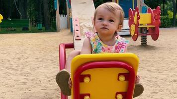 cute blonde caucasian toddler girl in dress with flower print plays on a playground video