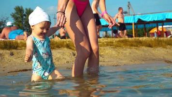 niña feliz corriendo en el agua y sostiene la mano de su madre. horario de verano en la playa con mamá e hija. video