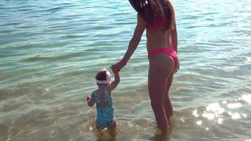 Beautiful young slim mother in swimsuit walks with her baby girl on a beach video