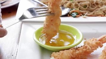 comida tailandesa, camarones empanados la mano de una mujer está usando un tenedor para mojar los camarones y ponerlos en la salsa para mojar. video