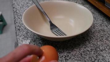 la mano del chef está rompiendo un huevo en un recipiente a cámara lenta. Prepara un tenedor para hacer la tortilla. video