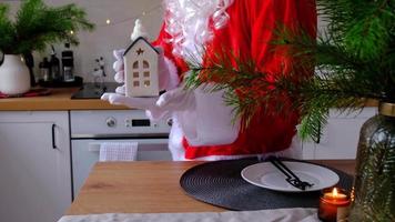 Hausschlüssel mit Schlüsselanhänger Häuschen in den Händen des Weihnachtsmanns im Freien im Schnee. Deal für Immobilien, Kauf, Bau, Umzug, Hypothek. gemütliches zu Hause. frohe weihnachten, neujahrsbuchungsveranstaltung und halle video