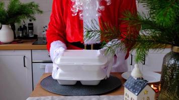 mat leverans till Hem service behållare i händer av santa claus sätter den på kök tabell och tar den bort. färdiggjorda varm ordning, jul, ny år högtider catering. video