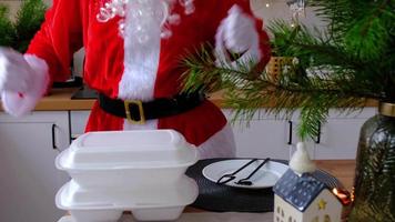Food delivery to home service containers on table and Santa Claus in kitchen cheerfully funny dansing. Ready-made hot order, Christmas, New year holidays catering. video