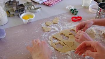 die hände von mutter und tochter schneiden kekse aus dem teig mit formen zu einem weihnachtsthema in form eines schneemanns, eines weihnachtsbaums, sterne aus video
