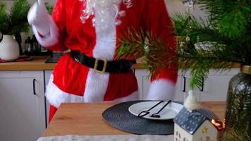 Santa Claus is having fun and funny dancing in the kitchen at Christmas at the dining table with an empty plate and appliances. Food delivery service, everyday life video