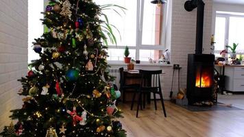 Festive interior of house is decorated for Christmas and New Year in loft style with black stove, fireplace, Christmas tree. Warm studio room with set table, burning wood, cozy and heating of home video