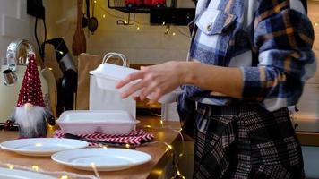 la mujer lo pone en la mesa y toma los contenedores del servicio de entrega de alimentos en la mesa cocina festiva escandinava blanca con decoración navideña. víspera de año nuevo, ahorrando tiempo, demasiado perezoso para cocinar, pedido caliente, caja de plástico video