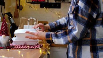 Woman puts it on table and takes food delivery service containers on table white scandi festive kitchen in christmas decor. Eve New year, saving time, too lazy to cook, hot order, plastic box video