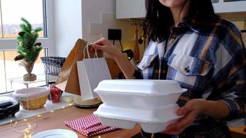 la mujer lo pone en la mesa y toma los contenedores del servicio de entrega de alimentos en la mesa cocina festiva escandinava blanca con decoración navideña. víspera de año nuevo, ahorrando tiempo, demasiado perezoso para cocinar, pedido caliente, caja de plástico video