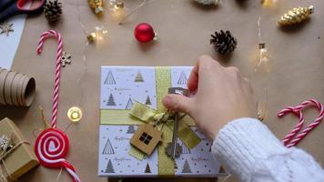 Key to house with keychain on cozy home in gift box with Christmas decor packaging. Pack present for New Year, Christmas. Building, project, moving to new house, mortgage, rent, purchase real estate video